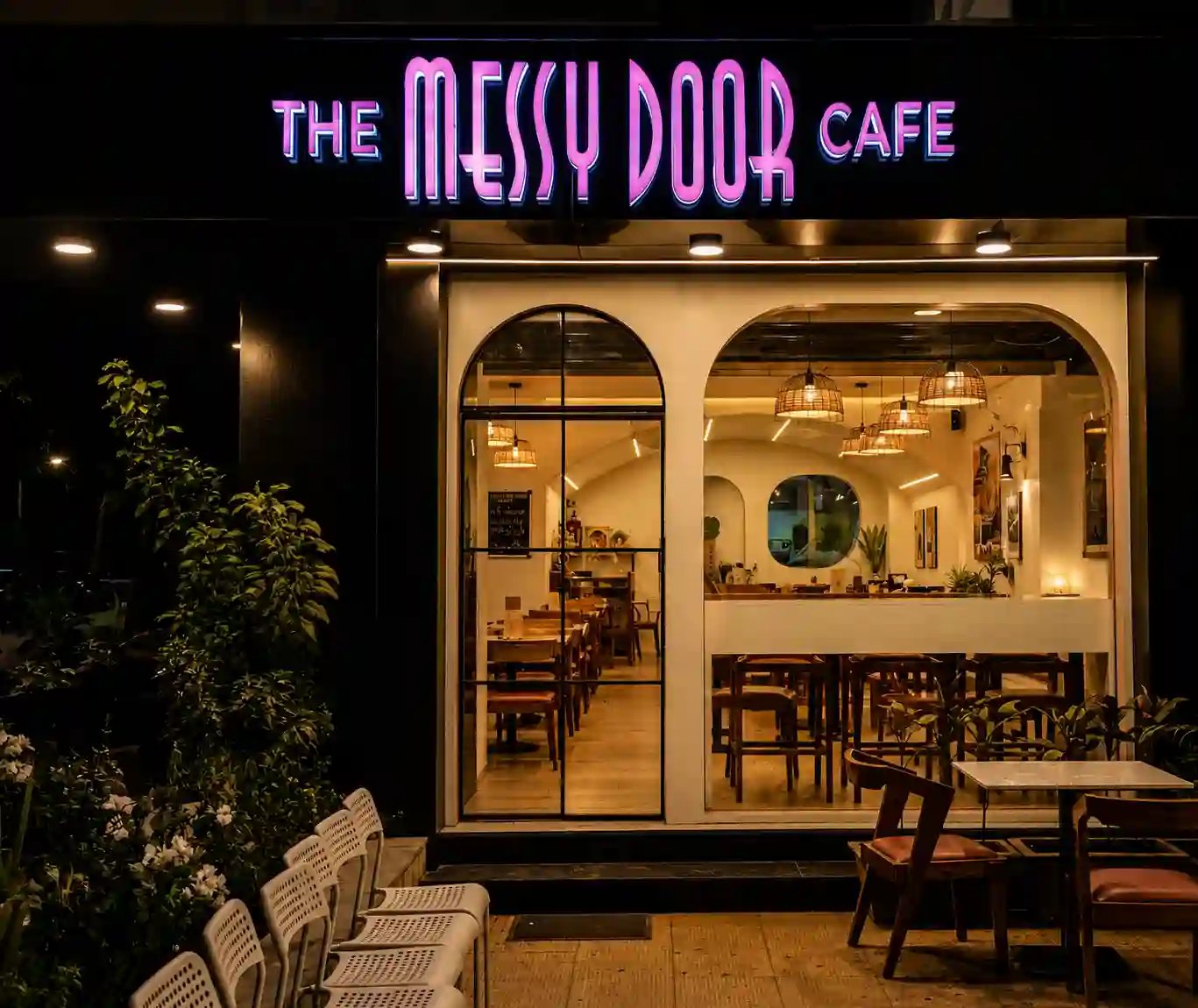 Glowing pink neon sign and arched windows of The Messy Door Cafe on HL College Road Ahmedabad